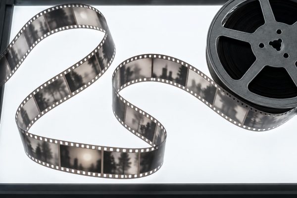 Tira de película de 35 mm desenrollada sobre una mesa de luz junto a una bobina metálica, vista desde arriba