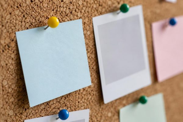 Primer plano de un tablón de corcho con tarjetas en blanco sujetas con chinchetas de colores